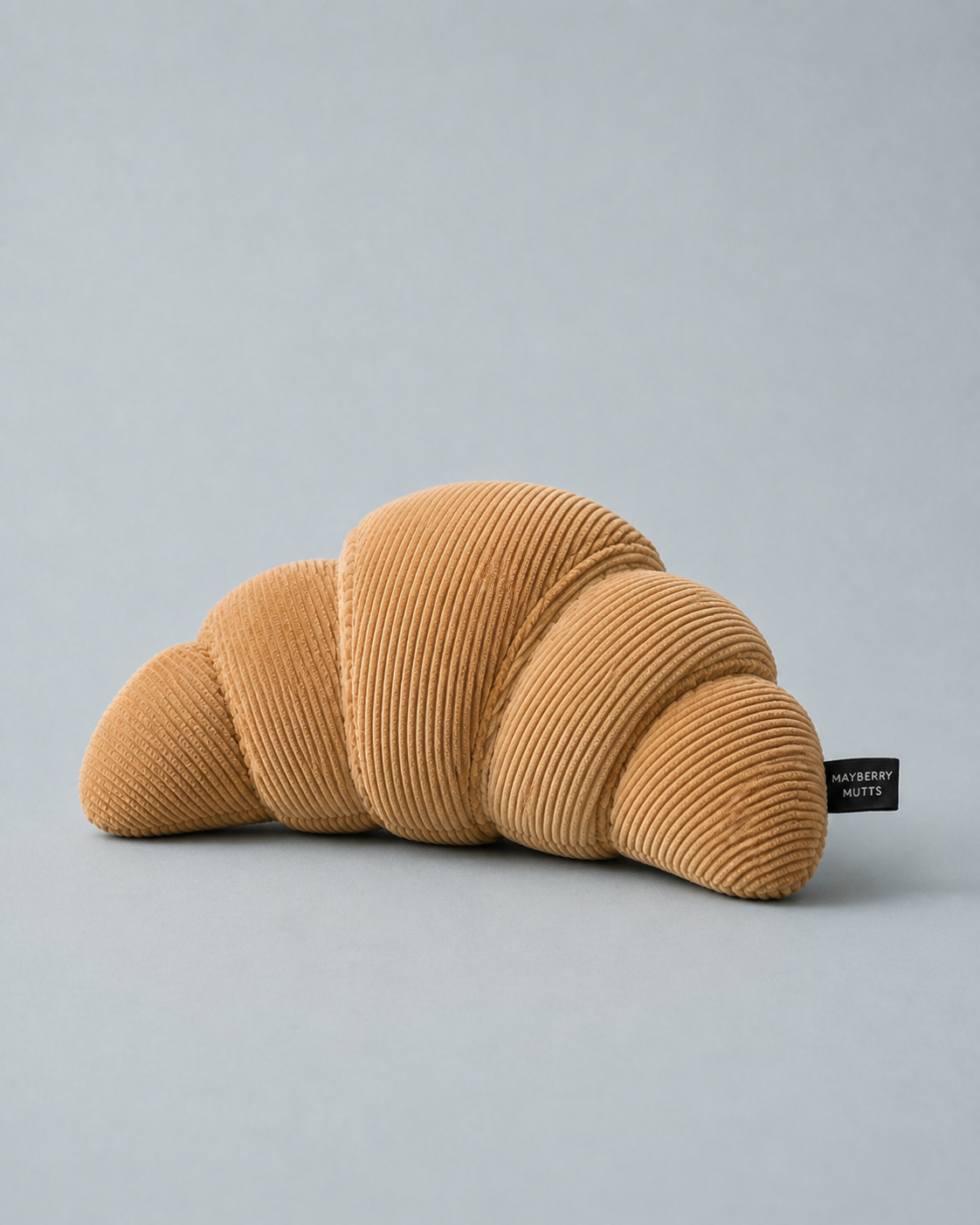 Corduroy Croissant Plush Dog Toy — tan ribbed corduroy plush shaped like a croissant, with woven Mayberry Mutts tag